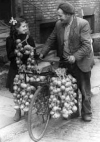 Onion seller with garlands of onions slung over his bicyle talking to woman